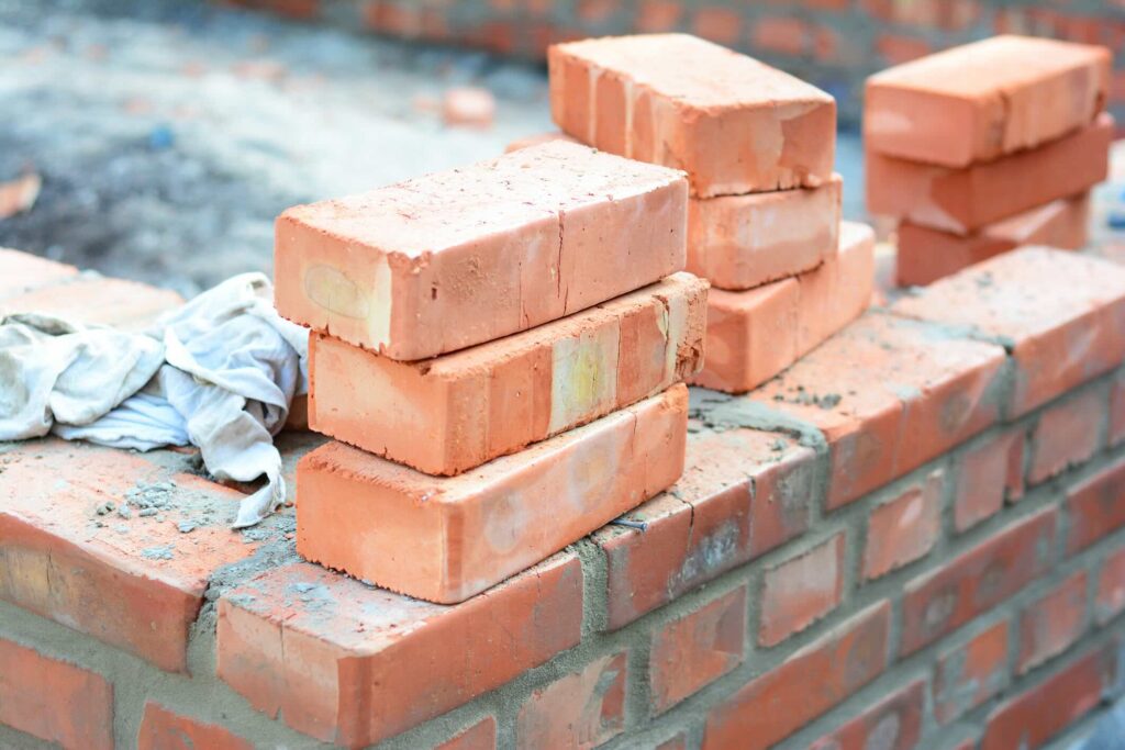 Three stacks of three red bricks sit on top of an in-progress brick foundation.