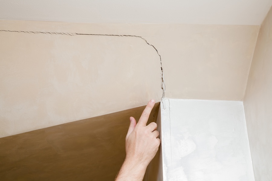 Man's hand finger pointing to the cracked wall in house.