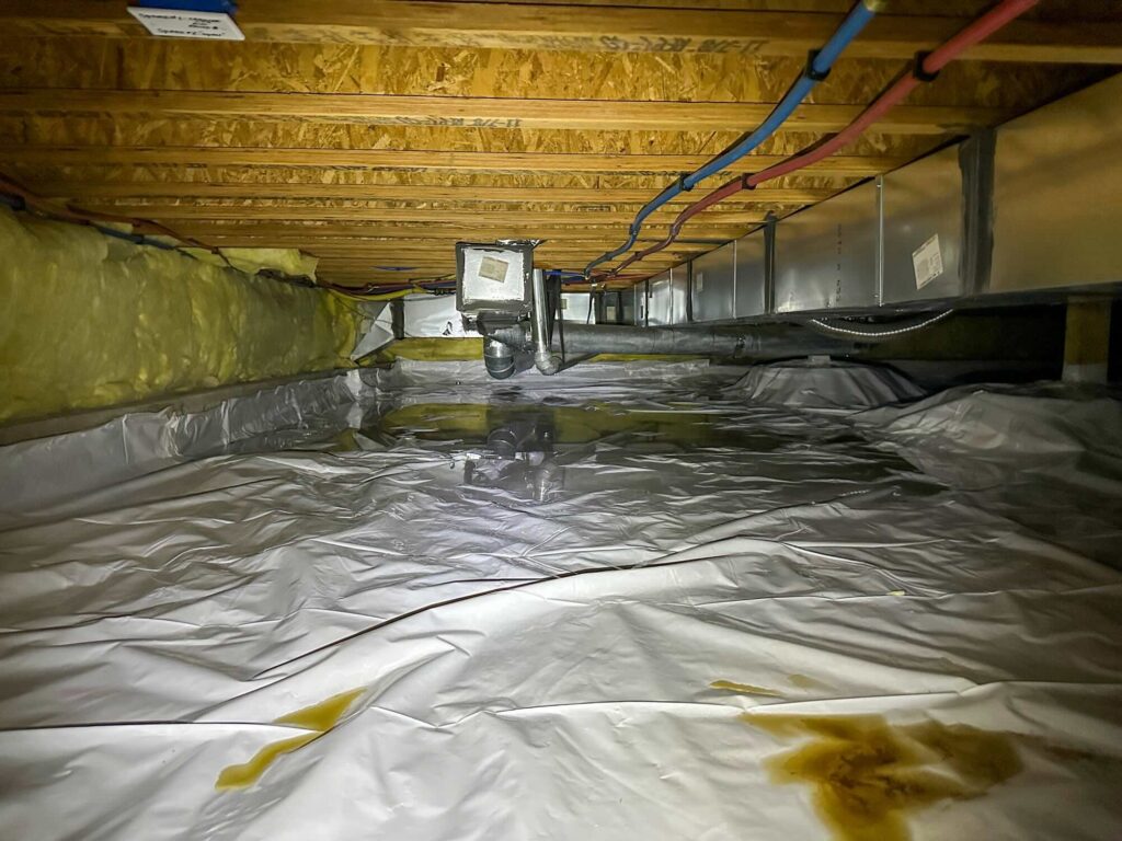 A wide angle shot of a crawlspace after a water loss with standing water on the vapor barrier