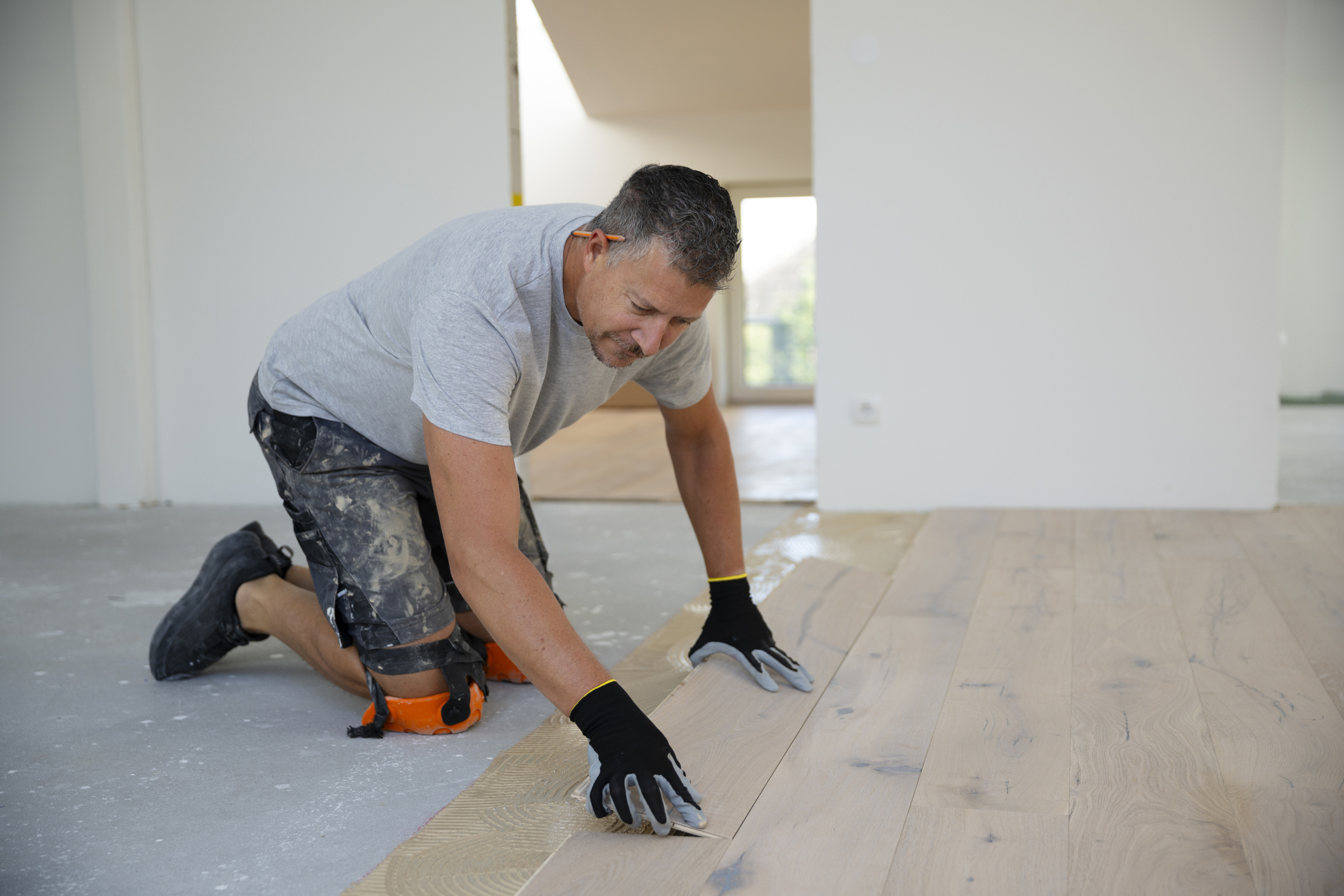 Middle-aged man working on floor, laying parquet floor in loft apartment