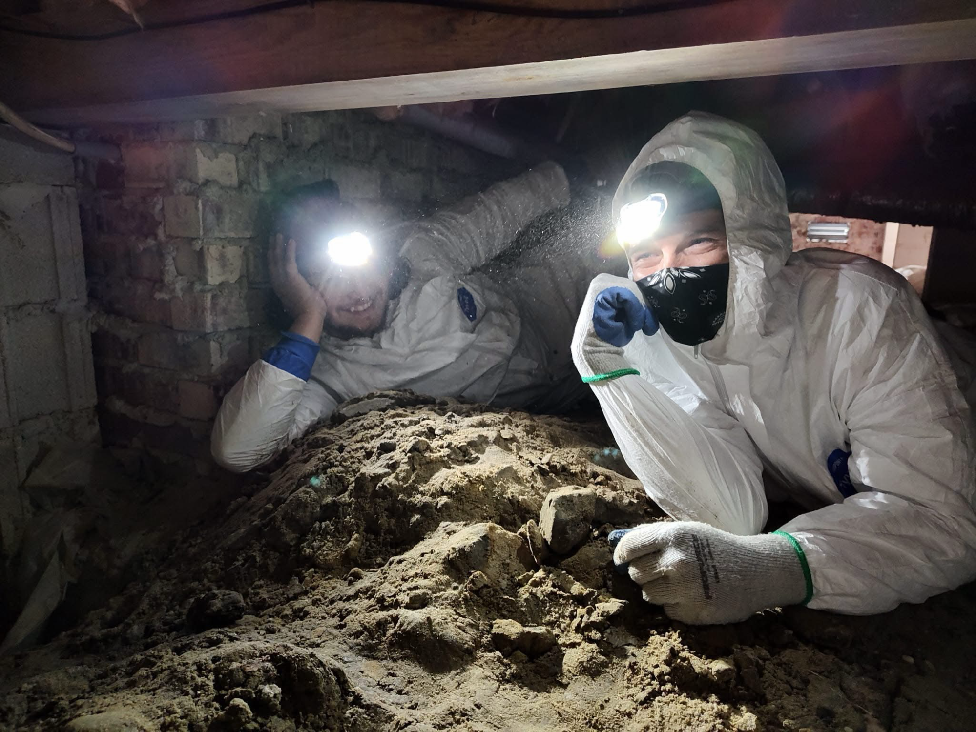 Two men working in a crawl space holding a flashlight