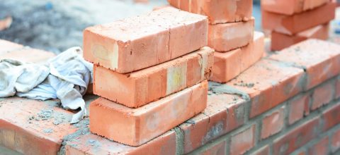 Three stacks of three red bricks sit on top of an in-progress brick foundation.