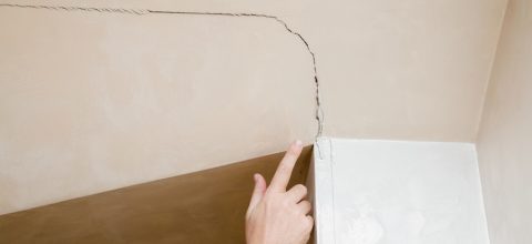 Man's hand finger pointing to the cracked wall in house.