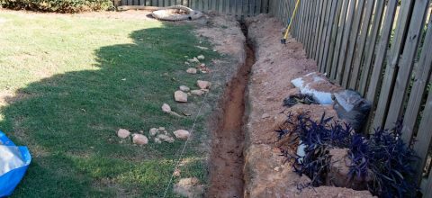 Trench excavated through a backyard of red clay for the DIY installation of a french drain.