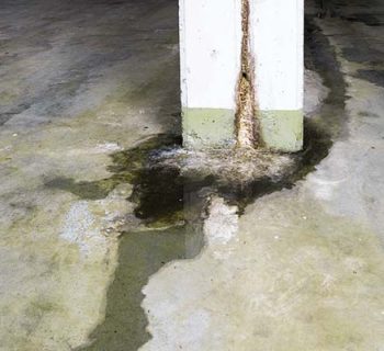 water damage in concrete construction with calcium and rust deposits and puddles near a supporting wall pillar in a garage