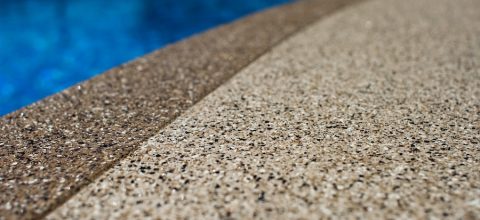 A closeup of a decorative concrete overlay, next to a blue swimming pool.
